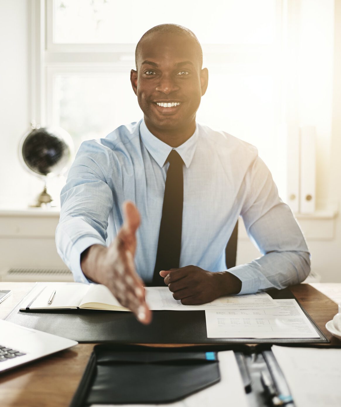 Smiling young executive sitting at his desk extending a handshake